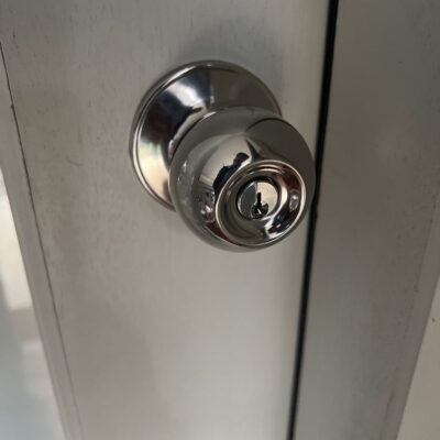 Close-up of a metal door knob with an integrated keyhole on a white wooden door.