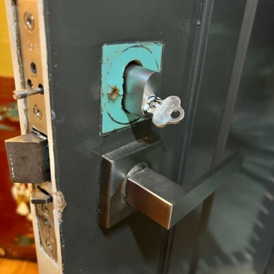 New lock barrel installed on dark-colored door with modern metallic handle and key inserted.