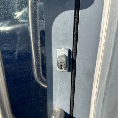 Close-up of a new lock barrel installed on a metal and glass office door with stainless steel handles.