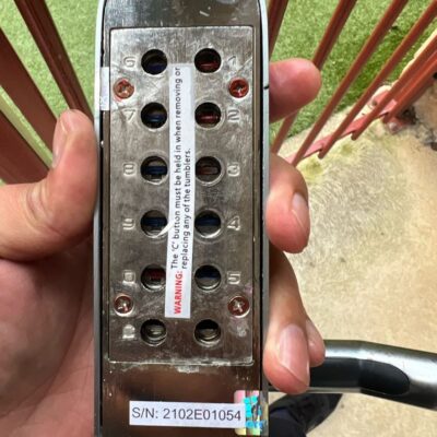 Close-up of a keypad entry lock showing numbered buttons, warning label, and serial number.