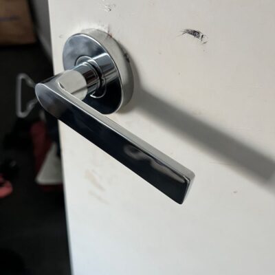 Newly installed modern metallic door handle on a white bedroom door with visible scratches around the installation area.