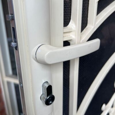 Close-up image of a security screen door lock with a white handle and keyhole.