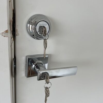 White door with chrome Kwikset deadbolt and entrance leverset, both with keys inserted.