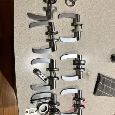 Several silver door levers and hardware parts laid out on a countertop, indicating preparation for a lock change.