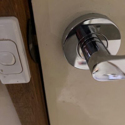 Close-up of a chrome leverset door handle and adjacent light switch on a wooden frame.
