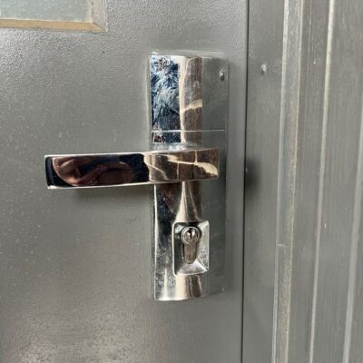 Close-up view of a metallic door lock on a grey door with visible handle and keyhole.