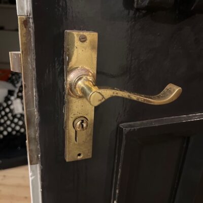 Old mortice lock with a key stuck in the barrel on a black-painted door.