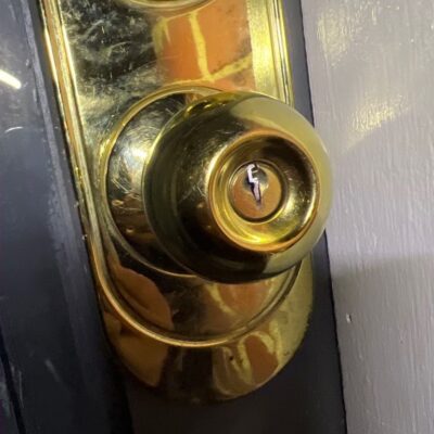 Close-up of a brass door lock with a broken key stuck in it on a white-painted door.
