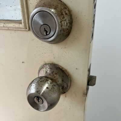 Old and rusted door lock and knob on a partially open door.