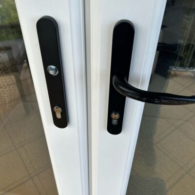 Close-up of a broken door lock handle on a white double door with black handles.