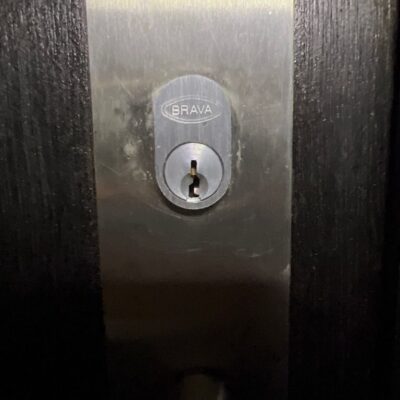 Close-up image of a BRAVA door lock on a dark-colored door.