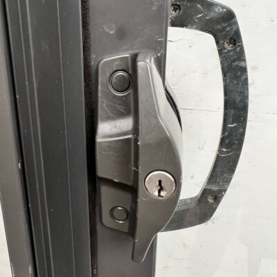 Close-up of a re-keyed sliding door lock with a keyhole and handle on a dark-colored frame.